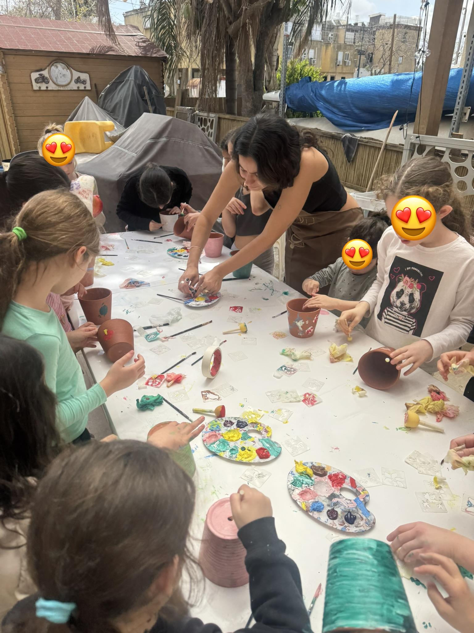 מדריכה עובדת עם קבוצת ילדים גדולה בצביעת כלי חרס — פעילות יצירה ליום כיף לילדי עובדים